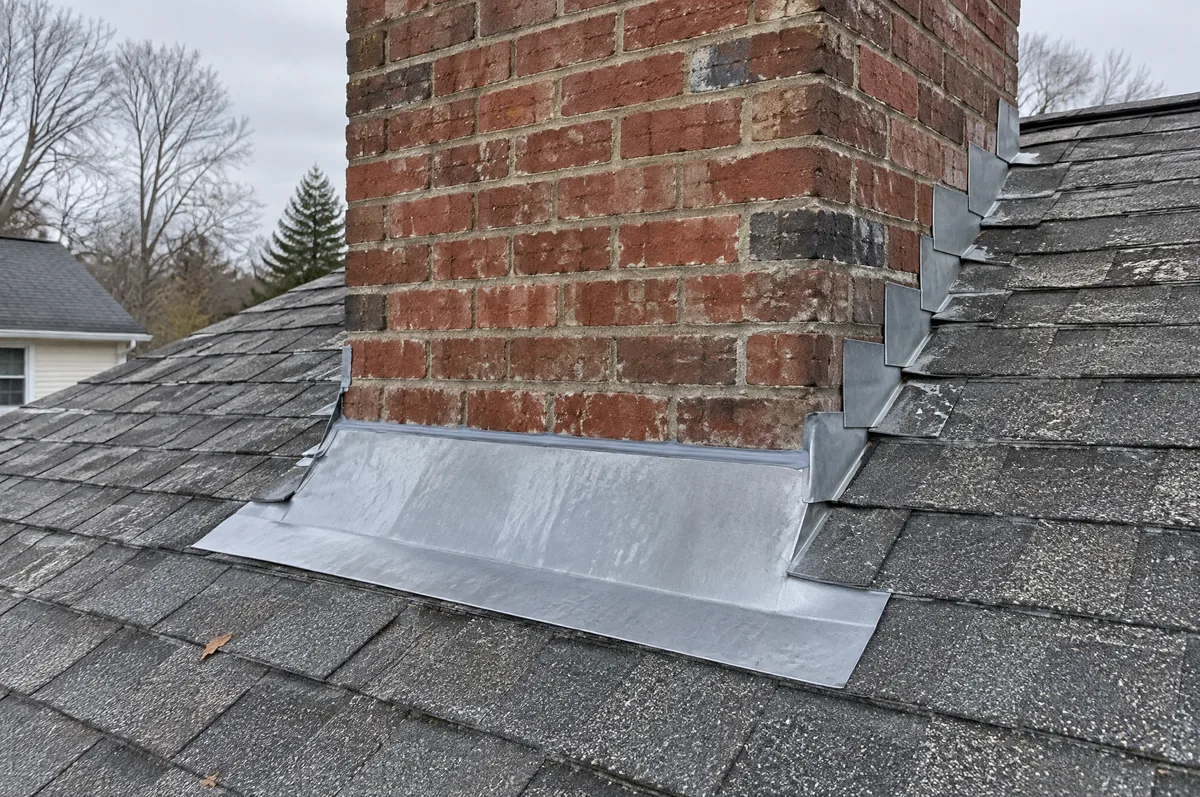 Step flashing and counter flashing where a brick chimney meets a shingle roof