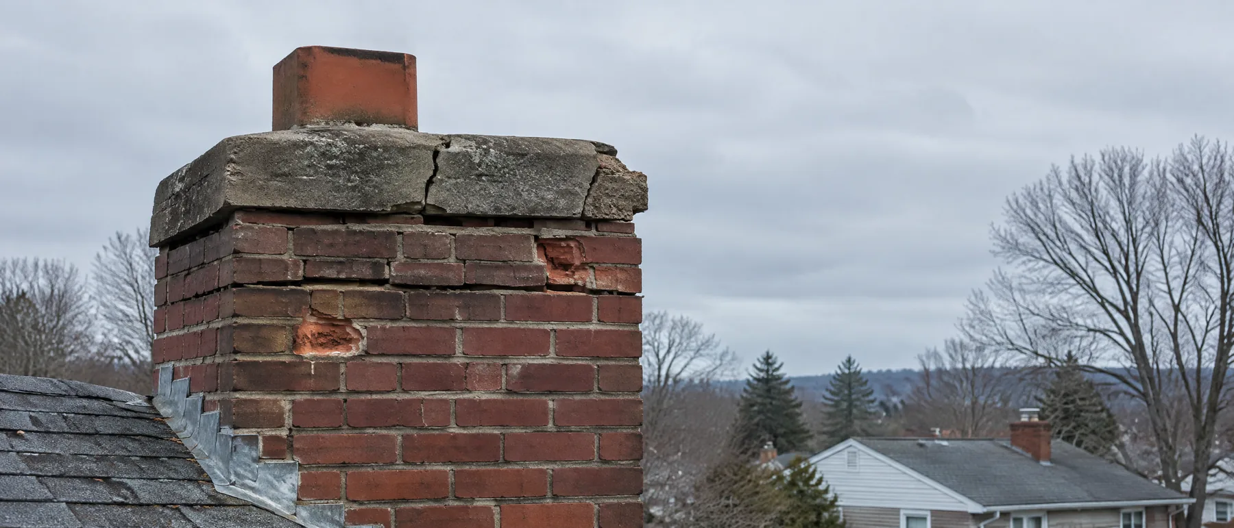Weathered brick chimney with a cracked crown against an overcast sky